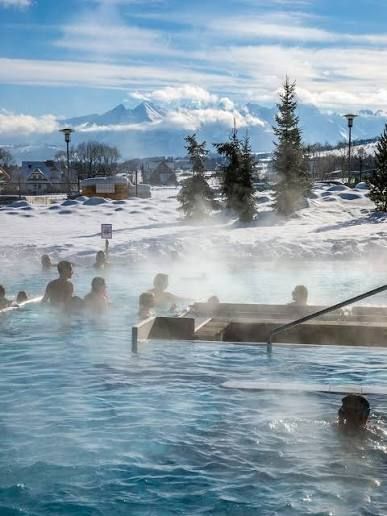 A WeRoad group trip of people soaking in a steaming outdoor thermal pool surrounded by snow and mountains.
