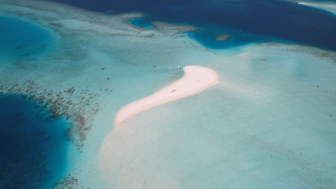 Vista aerea di una lingua di sabbia bianca curva circondata da limpide acque oceaniche turchesi e barriere coralline