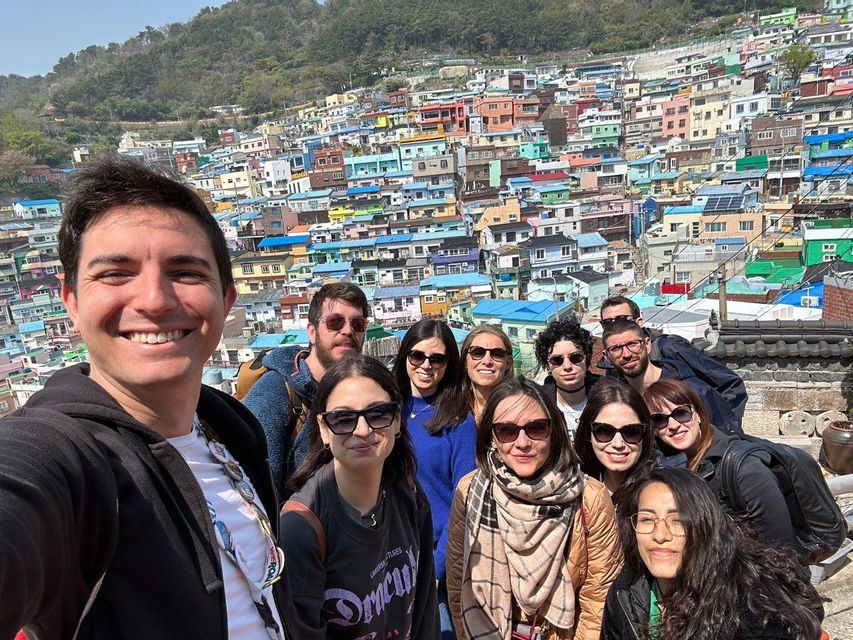 Un uomo si scatta un selfie sorridente con un viaggio di gruppo WeRoad davanti a un villaggio collinare con case colorate.