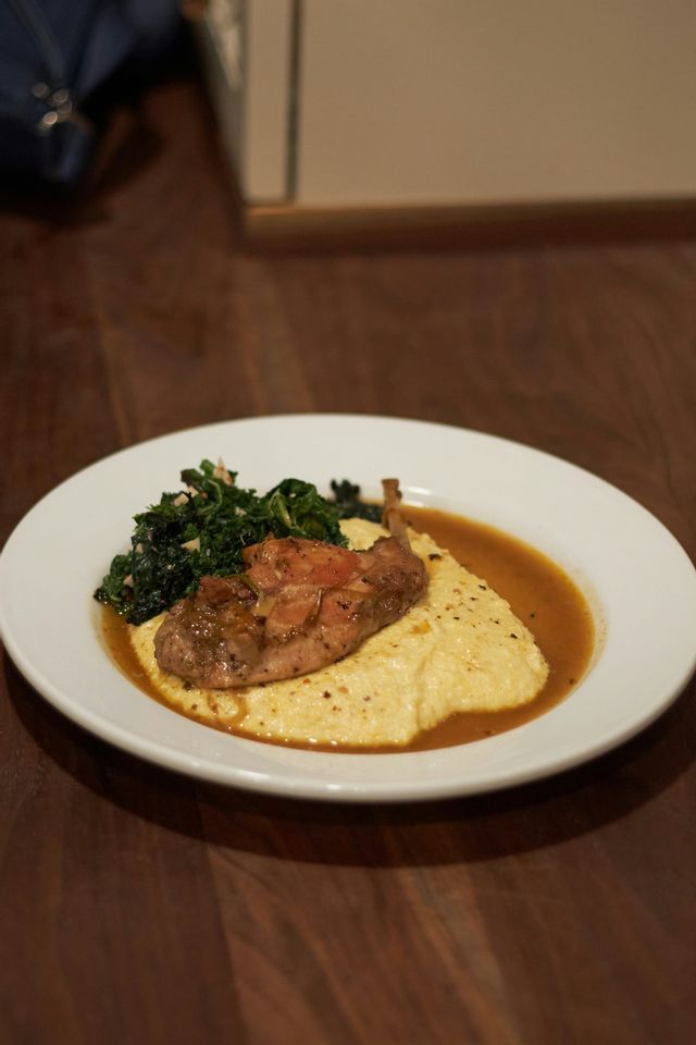 Un piatto di carne arrostita servita su polenta cremosa con verdure saltate e sugo su un tavolo di legno
