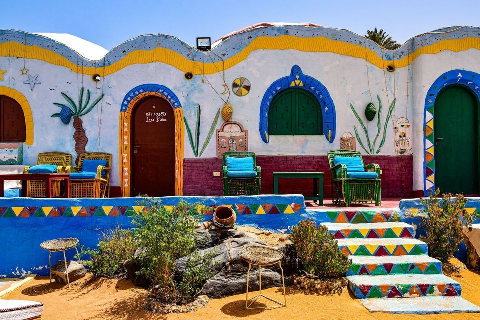 Facciata di edificio colorata e vivacemente dipinta con sedie da patio esterne e gradini in pietra geometricamente decorati.
