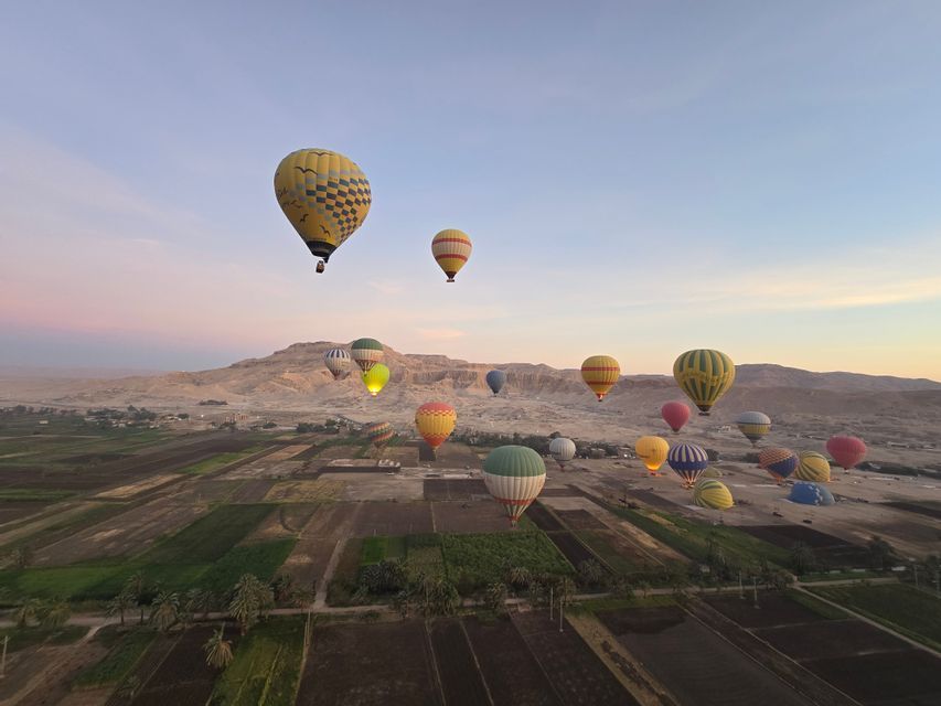Colorate mongolfiere fluttuano su campi coltivati e colline aride sotto un dolce cielo mattutino