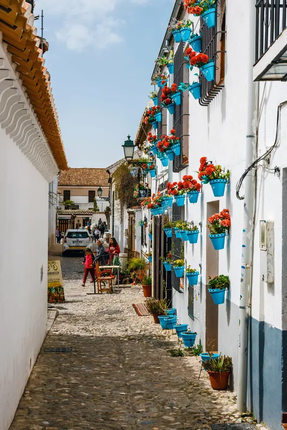Una calle estrecha empedrada bordeada de casas encaladas decoradas con macetas de flores azul brillante en las paredes