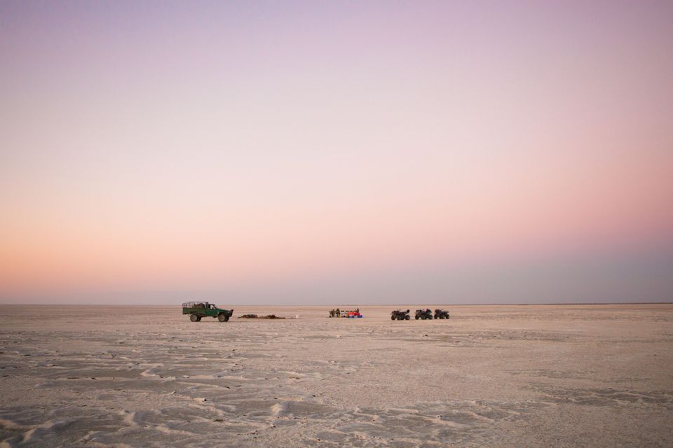 Un viaggio di gruppo WeRoad in pausa su una distesa di sale desertica con quad e un fuoristrada al tramonto