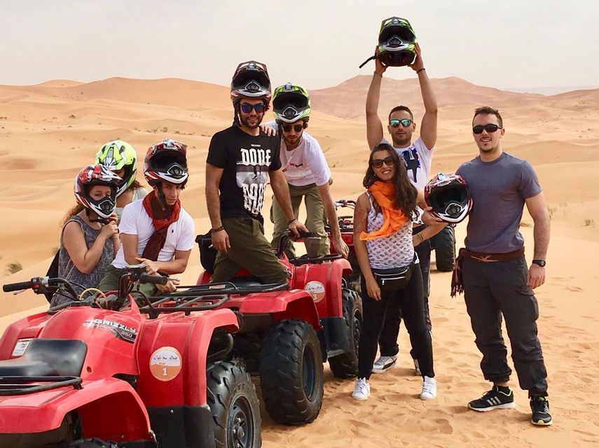 Un viaje en grupo de WeRoad posando para una foto con quads rojos y cascos en las vastas dunas de arena del desierto.