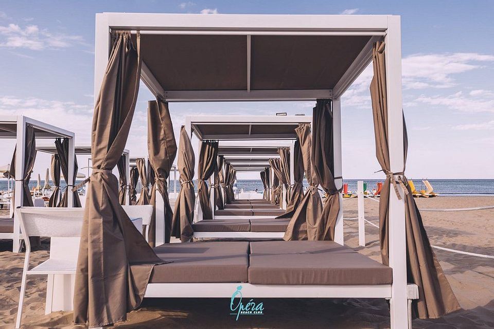 Una fila di cabine da spiaggia in legno bianco con tende e lettini imbottiti su una riva sabbiosa sotto un cielo luminoso