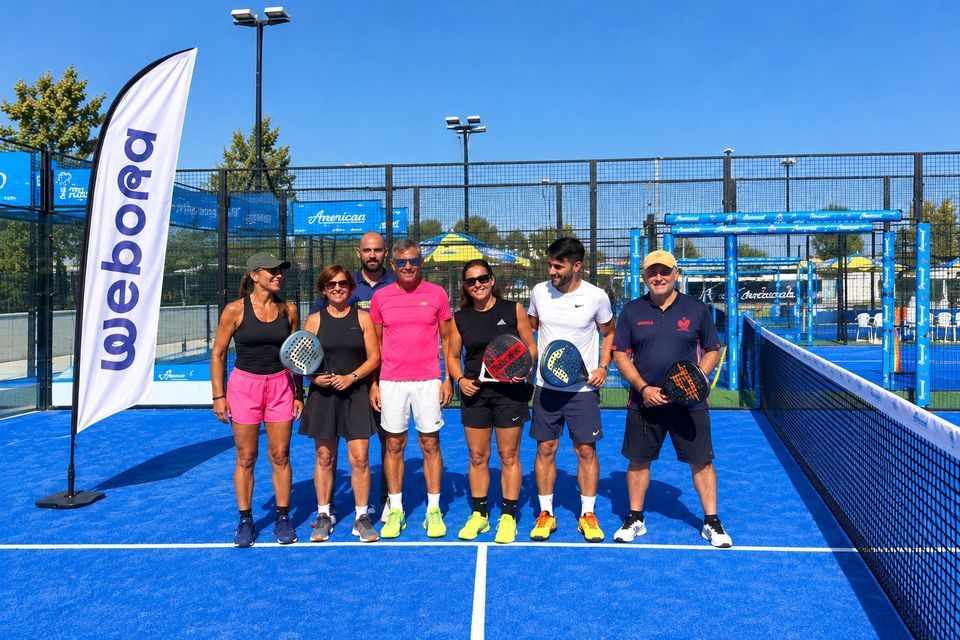 Un gruppo di giocatori di padel in posa con le racchette su un campo all'aperto blu brillante sotto un cielo sereno