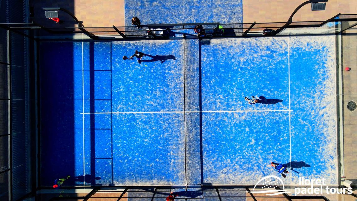 Vista aerea dall'alto di persone che giocano una partita su un campo da padel all'aperto blu vibrante.