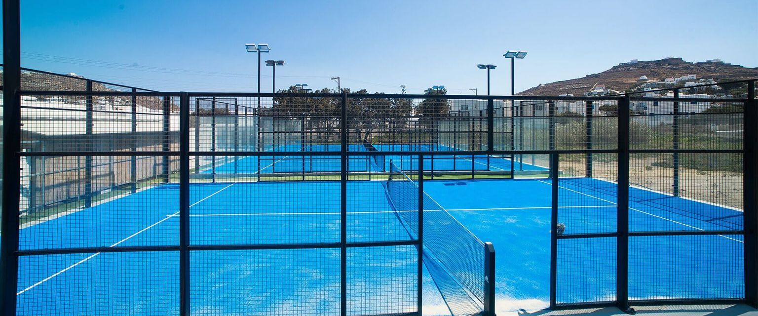 Campi da padel blu esterni vuoti recintati da reti in metallo nero sotto un cielo limpido e soleggiato