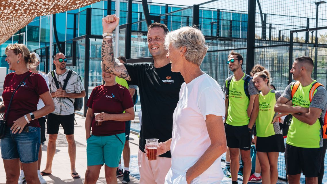 A WeRoad group trip smiling and celebrating together outdoors by a padel court on a sunny day.