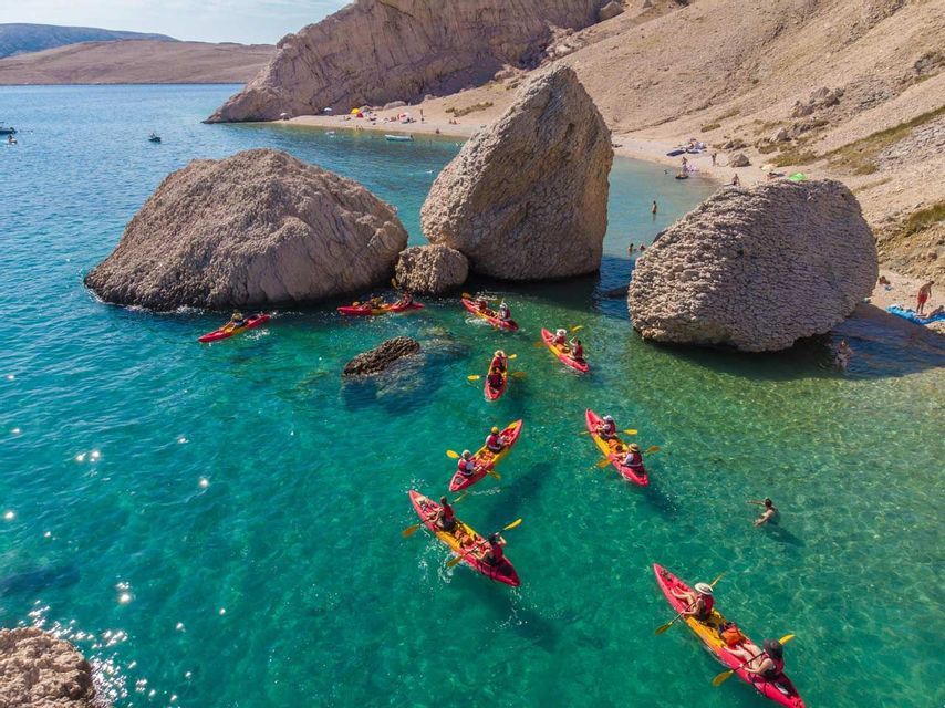 Un viaggio di gruppo WeRoad in kayak su canoe rosse attraverso limpide acque turchesi vicino a grandi massi e una spiaggia.