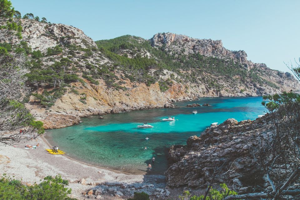 Eine Luftaufnahme einer abgelegenen Bucht mit klarem türkisfarbenem Wasser, wo mehrere Boote nahe einem Kieselstrand ankern.