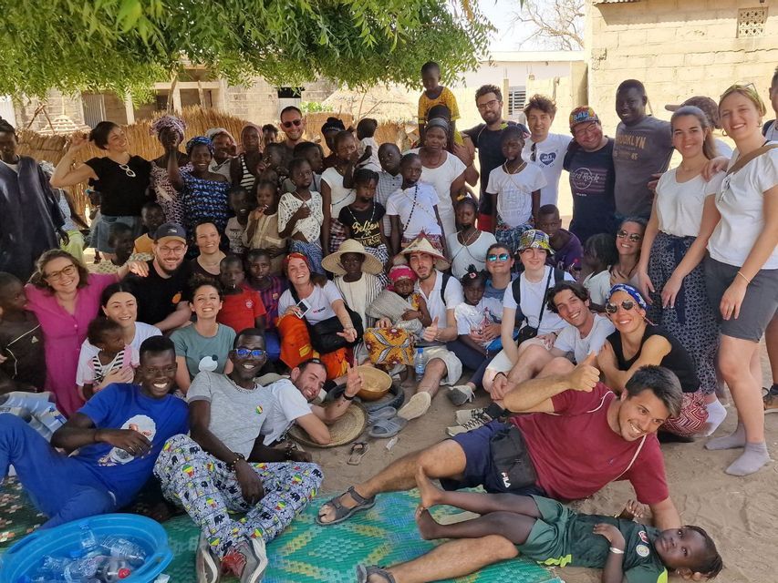 A WeRoad group trip and a local community with many children pose together for a photo in a village.