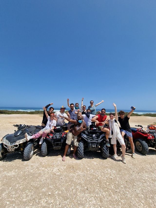 Un gruppo WeRoad in viaggio, in posa con i loro quad su un sentiero sterrato e l'oceano sullo sfondo.