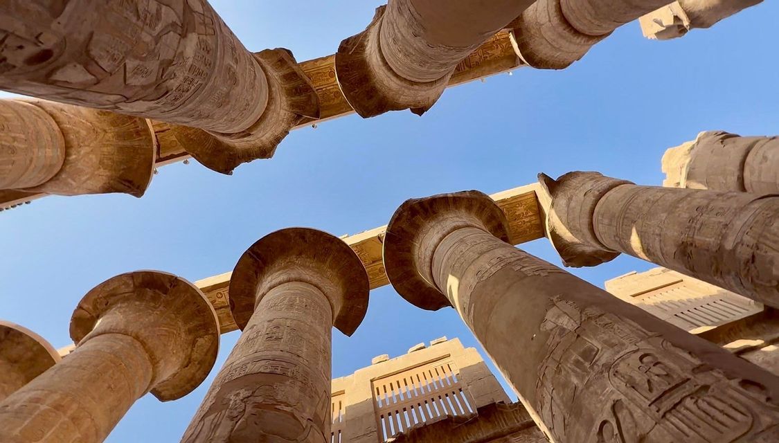 Inquadratura dal basso di antiche colonne di pietra scolpite che si ergono verso un cielo azzurro e limpido in un tempio storico all'aperto