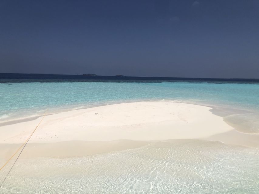 Una lingua di sabbia bianca si estende in acque limpide e turchesi sotto un cielo azzurro intenso, con l'oceano scuro all'orizzonte.