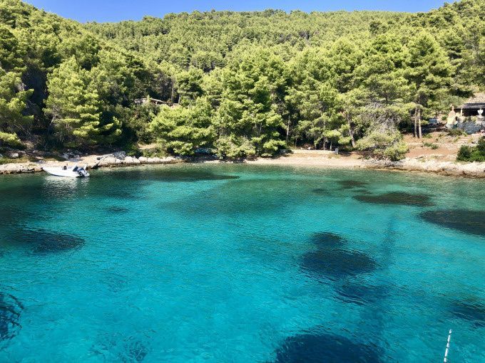A secluded cove with clear turquoise water, bordered by a dense pine forest and a small moored boat.