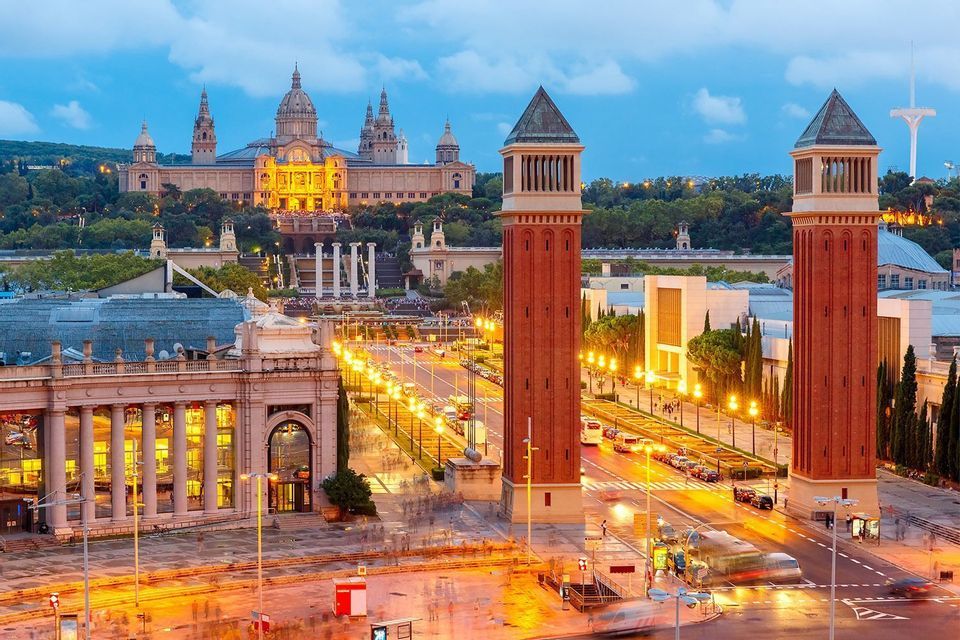 An evening cityscape featuring two large red brick towers, a bustling avenue, and an illuminated palace on a distant hill.
