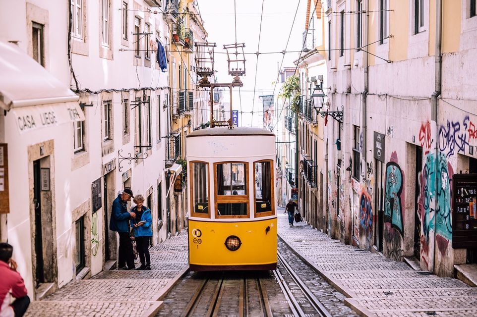 Un tram funicolare giallo sui binari al centro di una stretta e ripida strada acciottolata tra gli edifici.