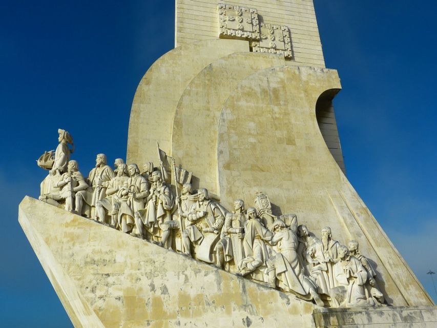 Un primo piano dal basso di figure storiche scolpite su un grande monumento in pietra contro un cielo azzurro chiaro.
