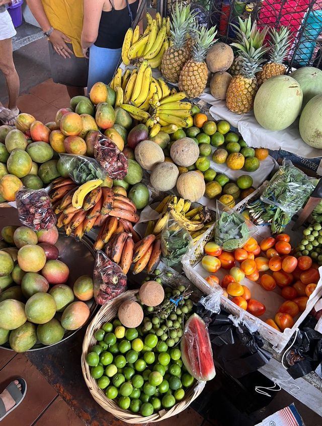 Eine Draufsicht auf einen Marktstand voller frischer tropischer Früchte wie Ananas, Bananen, Mangos und Melonen.