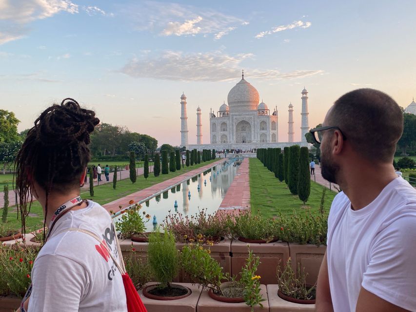Un uomo e una donna di un viaggio di gruppo WeRoad guardano il Taj Mahal e la sua vasca riflettente all'alba.