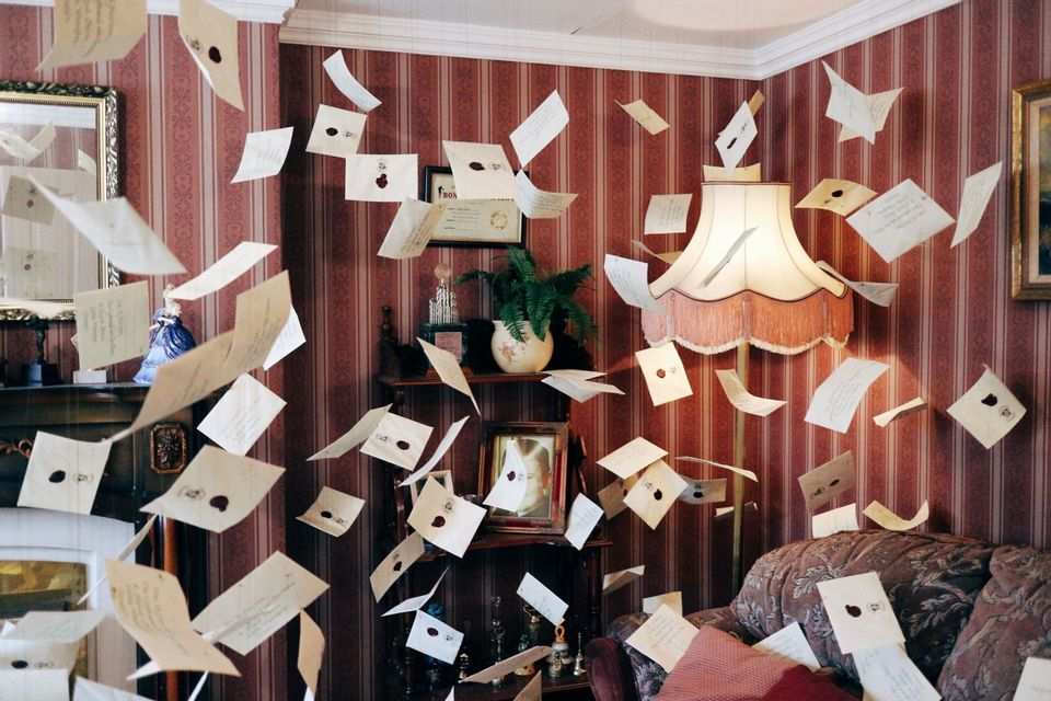 Numerose lettere e buste con sigilli in ceralacca fluttuano nell'aria all'interno di un salotto vintage con carta da parati a righe rosse.