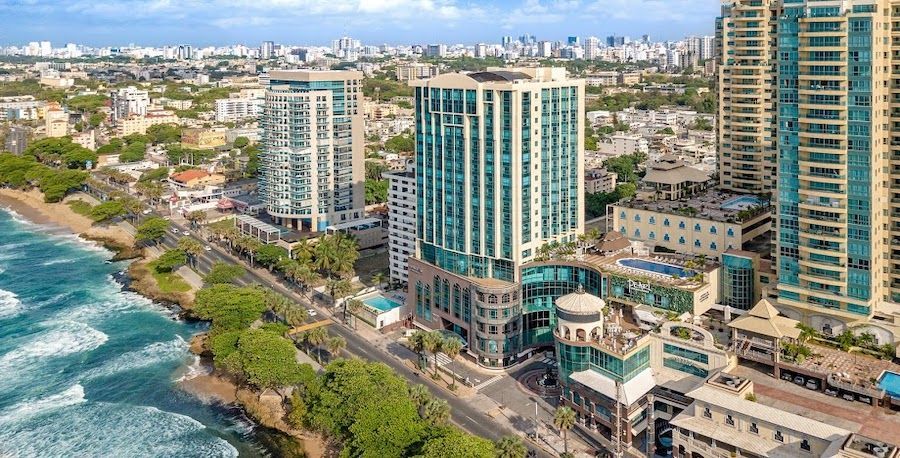 Veduta aerea di un moderno paesaggio urbano con hotel grattacielo che costeggiano una costa rocciosa accanto a un mare turchese.