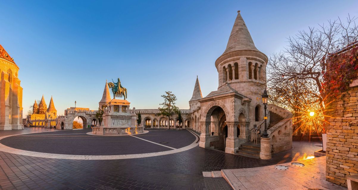 Una vista panoramica di un cortile di pietra vuoto con torri a torretta e una statua equestre all'alba.
