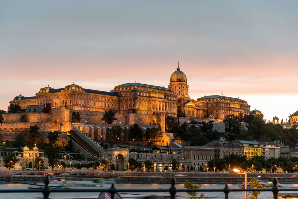 Palacio iluminado con gran cúpula en una colina sobre un río al atardecer.
