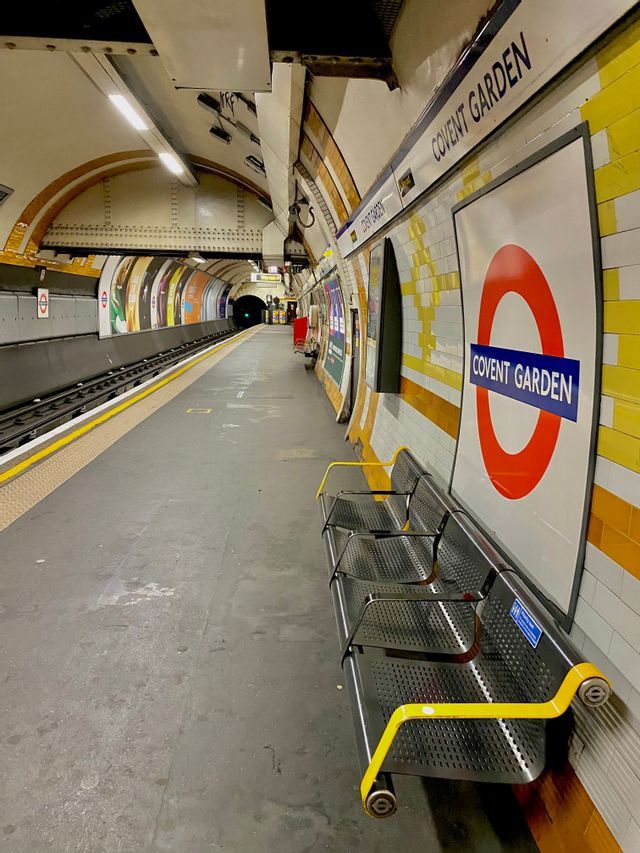 Vista lungo una banchina vuota della stazione della metropolitana di Covent Garden, con panchine in metallo e l'iconico segnale a tondo.