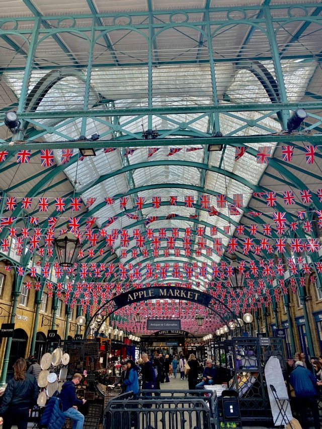 I visitatori passeggiano all'interno dell'Apple Market, sotto un tetto di vetro ad arco decorato con numerose bandierine britanniche.