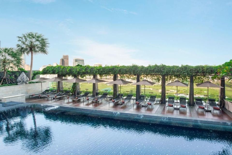 An outdoor swimming pool with lounge chairs on a wooden deck, overlooking a green field and a distant city skyline.