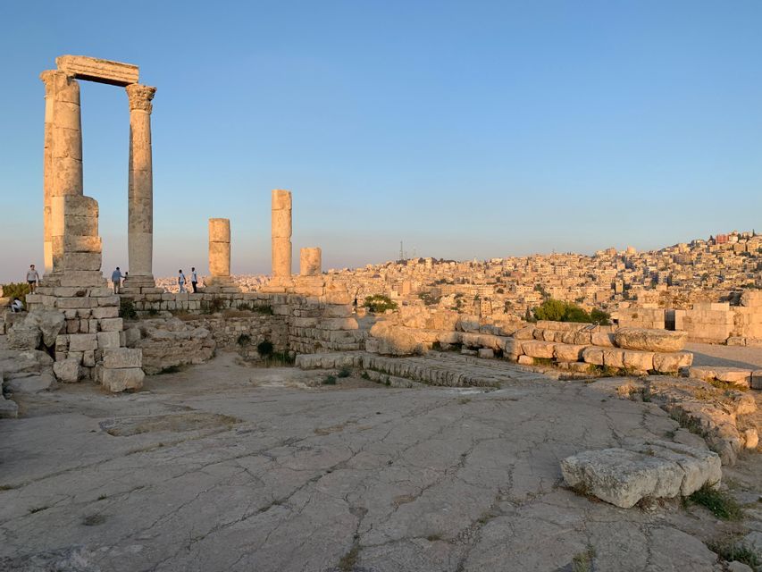 Un viaje en grupo de WeRoad se halla entre antiguas ruinas de piedra con altas columnas, con vistas a una extensa ciudad en una colina al atardecer.