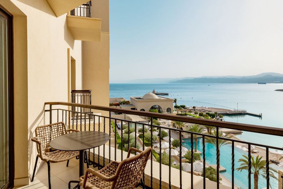 Vista dal balcone di un hotel con tavolo e sedie, affacciato su piscina, spiaggia e mare.
