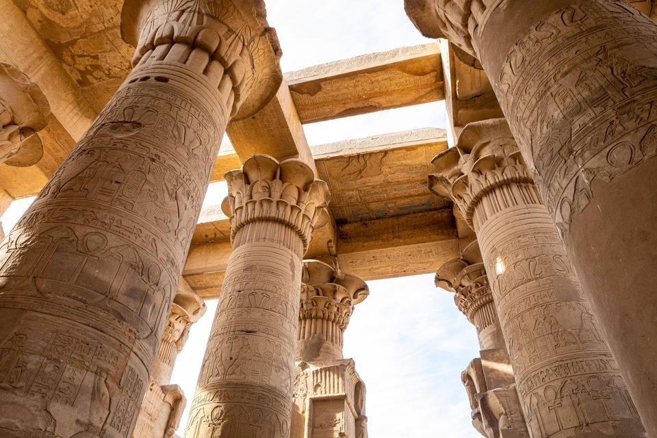Eine Untersicht auf große Steinsäulen mit geschnitzten Hieroglyphen in einem antiken Tempel, die eine Steindecke tragen.