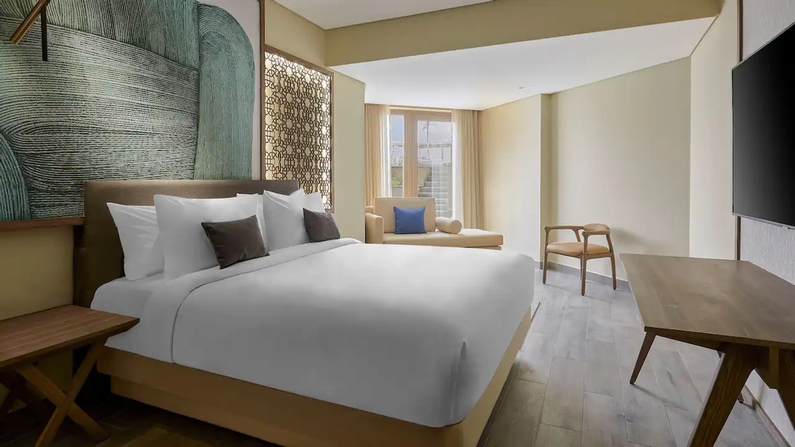 Ein Hotelzimmer mit einem ordentlich gemachten Kingsize-Bett, einem großen abstrakten grünen Kopfteil, einem Holzschreibtisch und einer Chaiselongue.