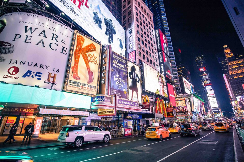 Cartelloni luminosi illuminano una trafficata via della città con taxi gialli, auto e pedoni di notte.