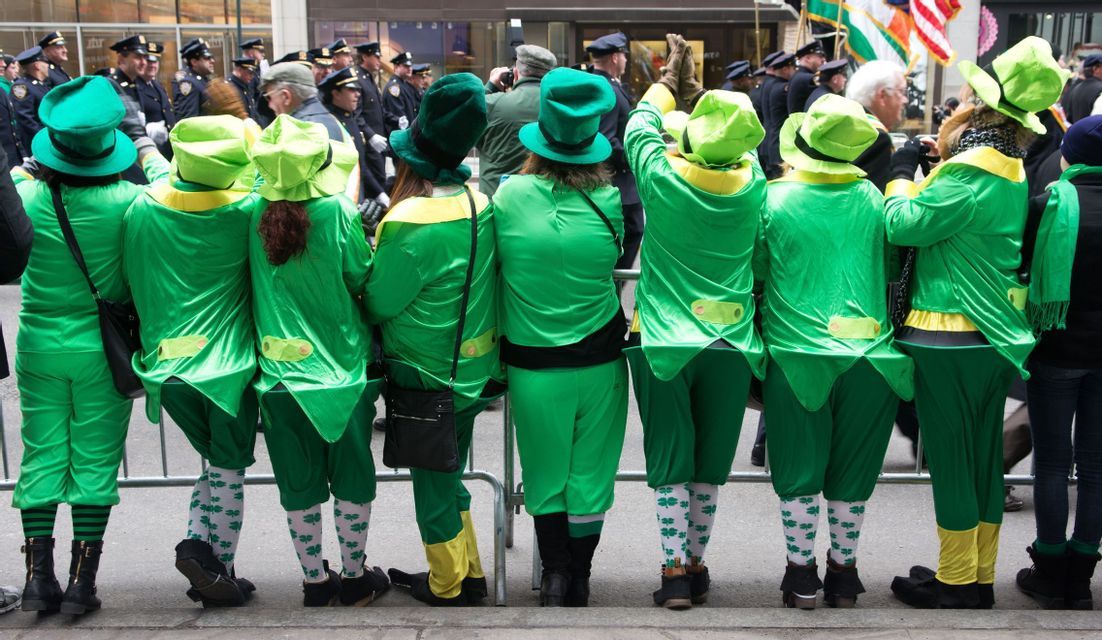 Da dietro, un gruppo di persone in costumi e cappelli verdi da folletto osserva una sfilata di strada.