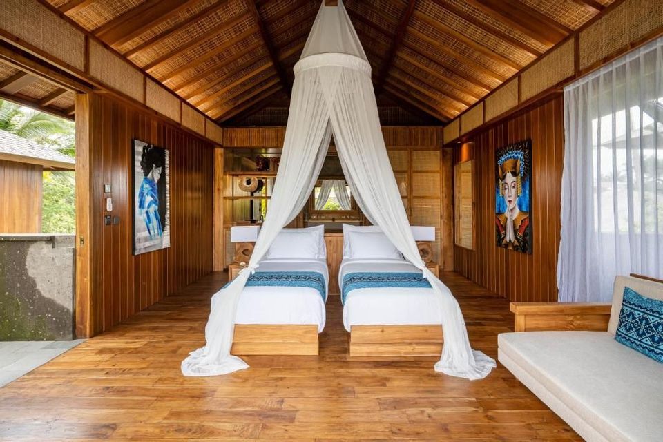 Geräumiges, holzgetäfeltes Schlafzimmer mit zwei Einzelbetten unter einem weißen Moskitonetz.