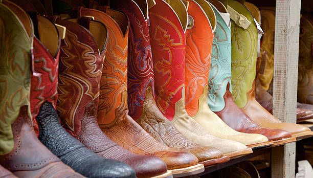Una fila di stivali da cowboy in pelle colorati e fantasia esposti su uno scaffale di legno.