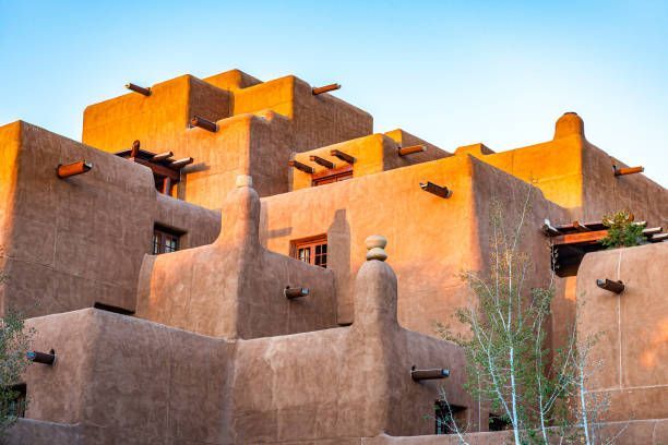 Un edificio a più livelli in stile adobe con travi in legno a vista è illuminato dalla luce dorata del sole contro un cielo sereno.
