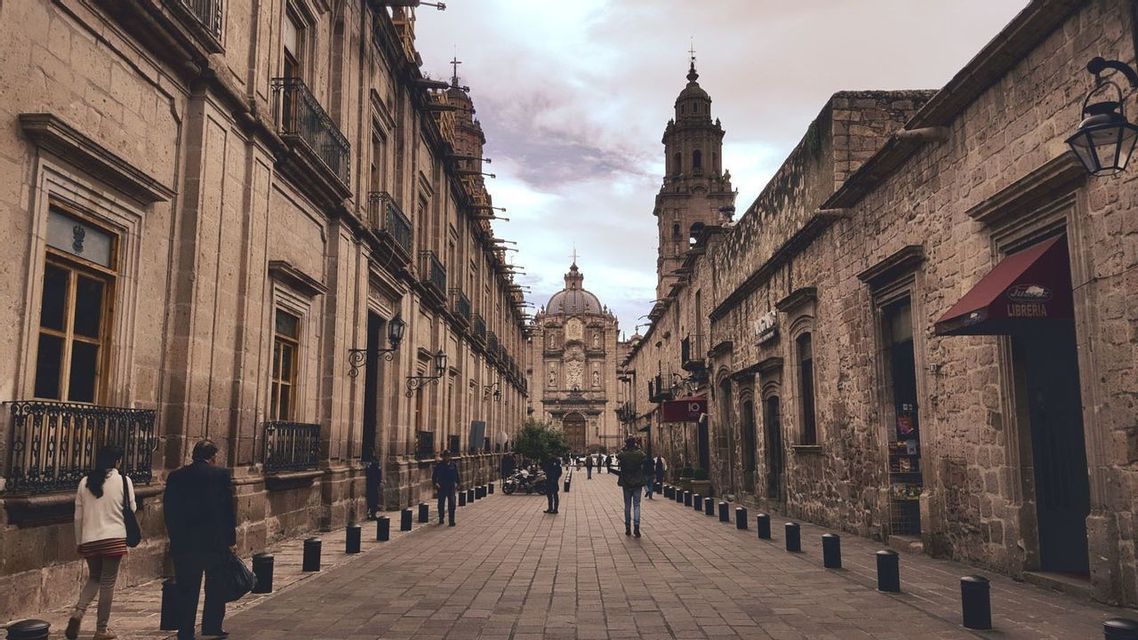 Una ancha calle adoquinada flanqueada por edificios históricos de piedra que conduce a una catedral bajo un cielo nublado.