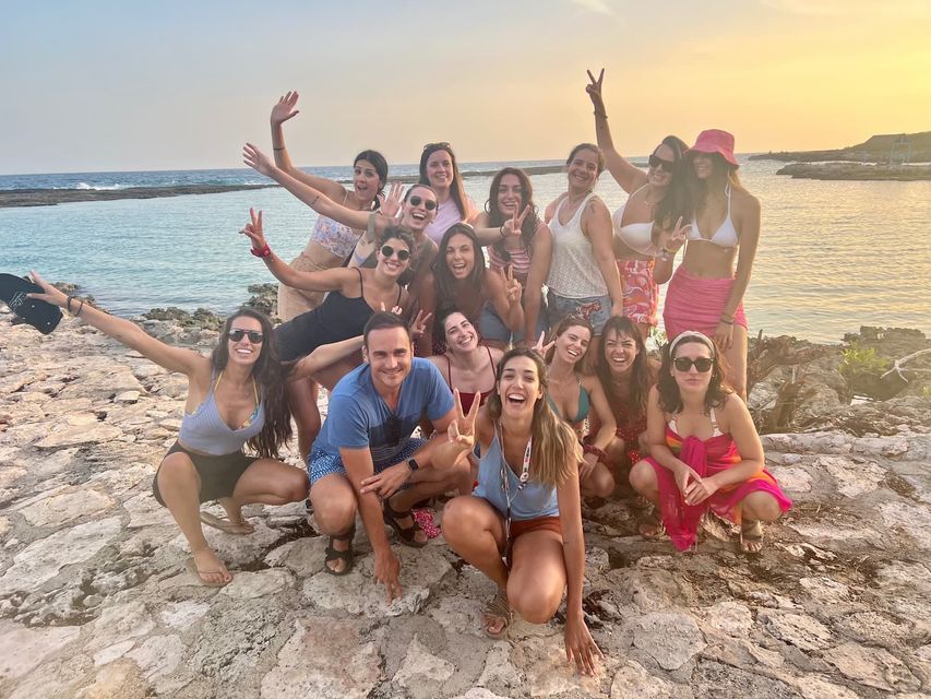 Un grupo de WeRoad de viaje sonríe y posa para una foto en una costa rocosa junto al mar al atardecer.