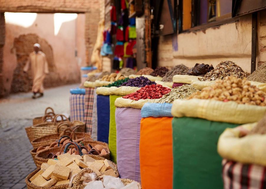 Des sacs colorés d'épices et d'herbes sont exposés à la vente sur un étal de marché extérieur dans une rue étroite.