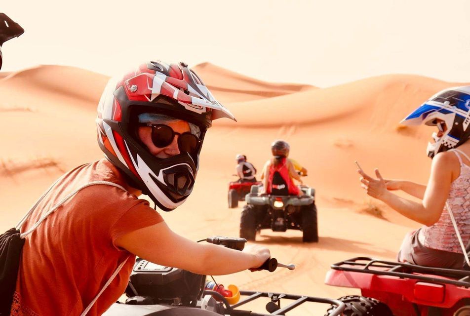 A WeRoad group trip wearing helmets and riding quad bikes across large desert sand dunes.