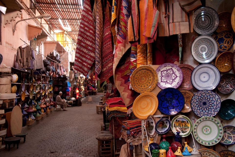 Une ruelle pavée étroite dans un marché couvert, avec des étals exposant des céramiques colorées, des tapis à motifs et d'autres articles.