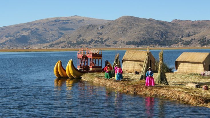 Persone in abiti tradizionali colorati su un'isola galleggiante di canne, vicino a capanne di paglia e una grande barca di canne su un lago.