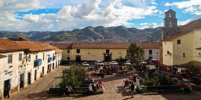 Una vivace piazza storica con bancarelle, circondata da edifici coloniali e una torre campanaria, con grandi montagne sullo sfondo.