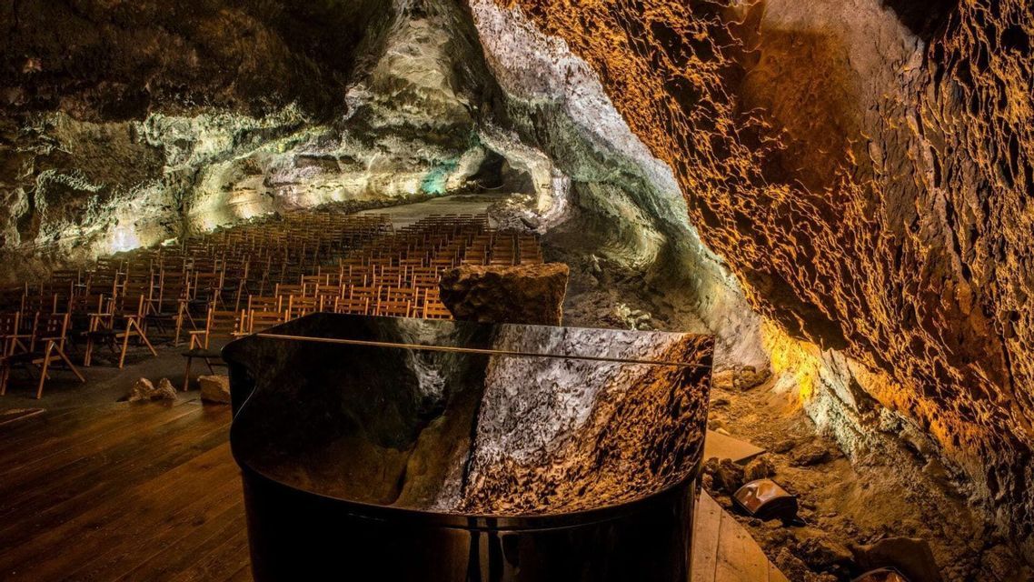 Una sala da concerto con un pianoforte a coda e file di sedie di legno allestita all'interno di una grande grotta naturale illuminata.